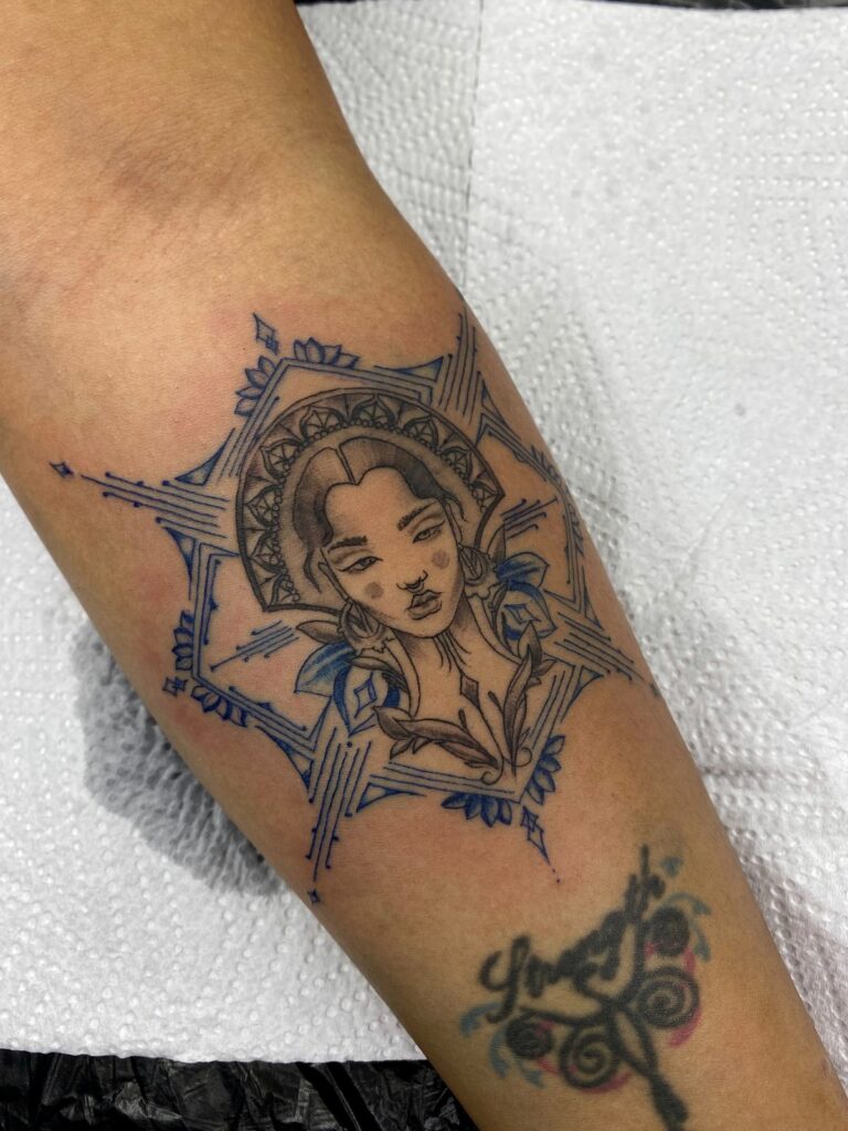 Fine-line portrait tattoo with an ornamental frame on the ankle