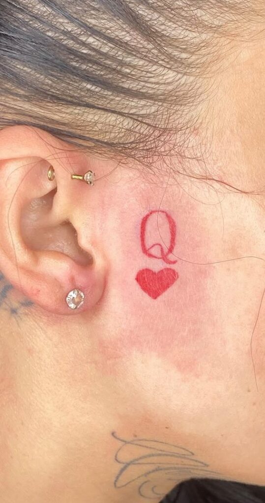 Small red initial and heart tattoo behind the ear